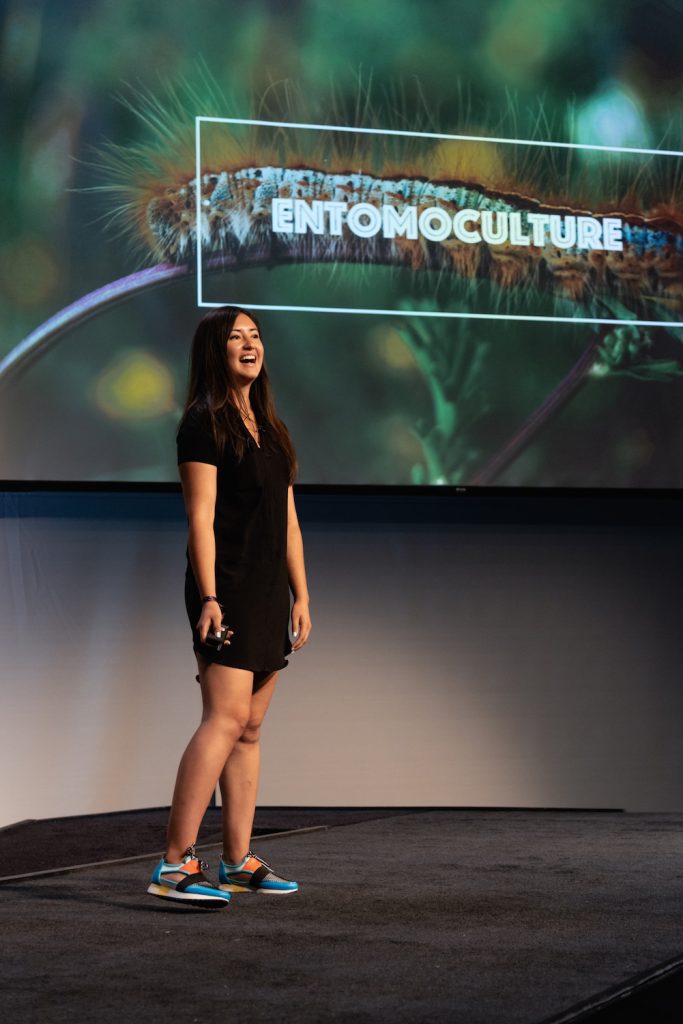 Natalie Rubio on stage presenting in front of a screen that says entomoculture